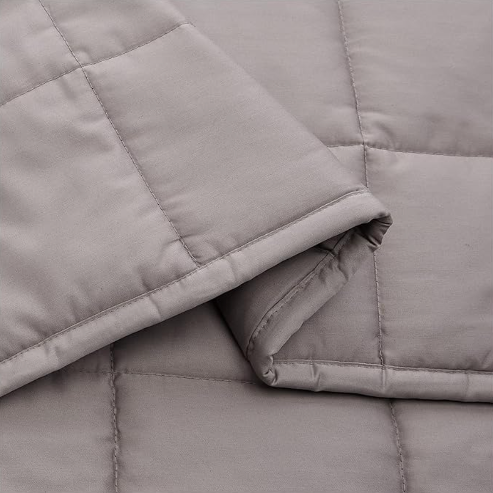 Gros plan d'une couverture lestée grise pliée avec piqûres carrées matelassées et finition coton douce