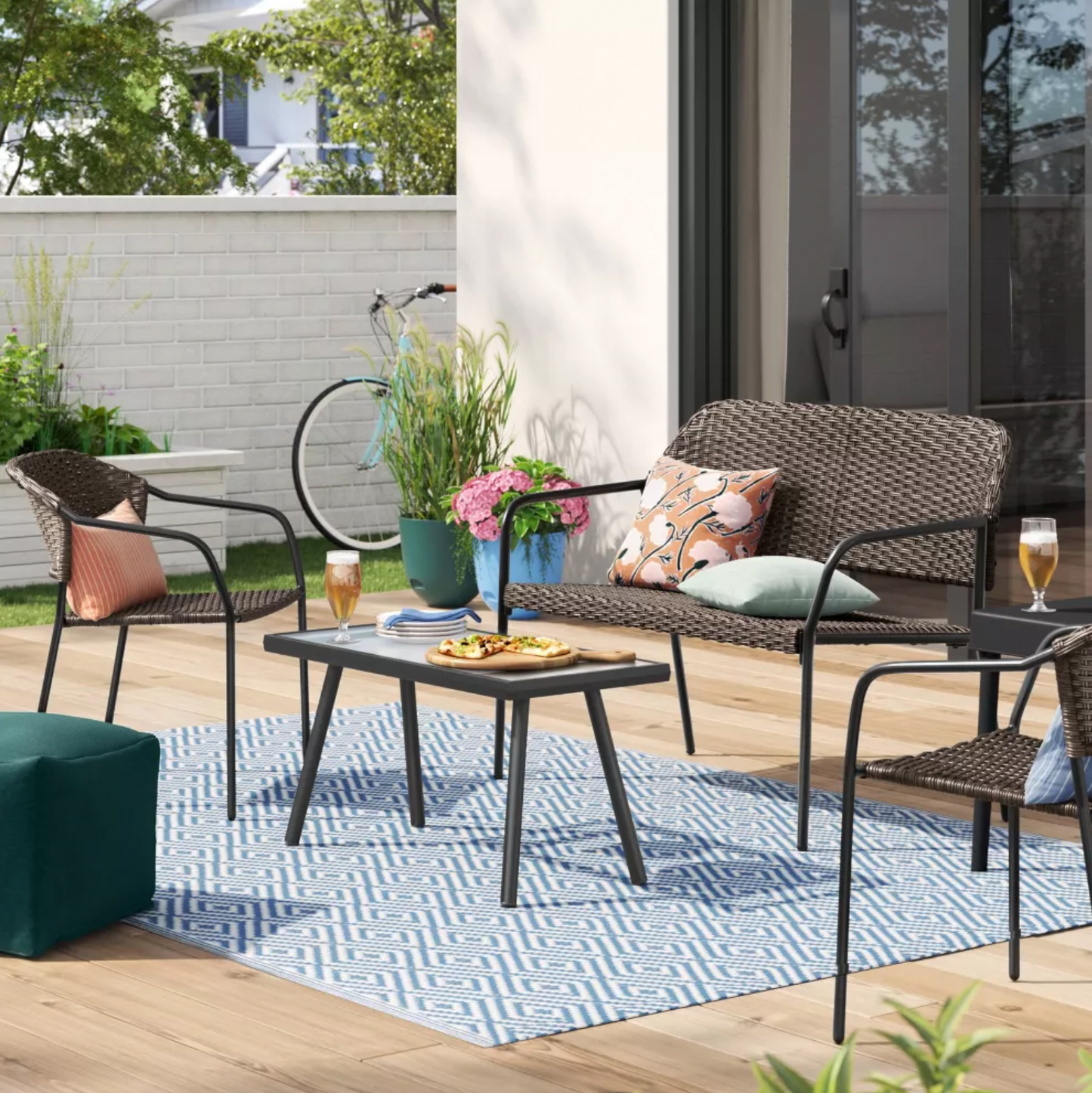 Table basse de patio rectangulaire à plateau en verre noir avec fauteuils et causeuse en osier sur terrasse en bois, scène lifestyle