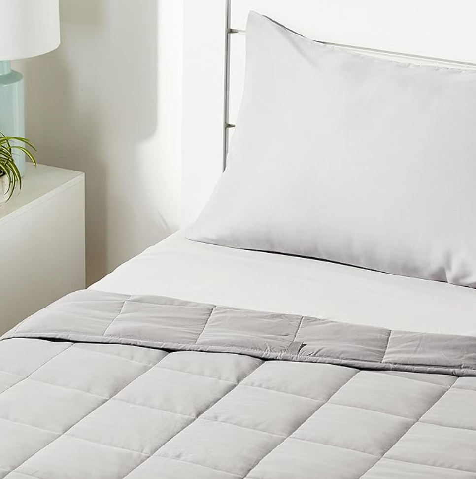 Couverture lestée grise matelassée pliée sur le lit dans une chambre avec linge blanc