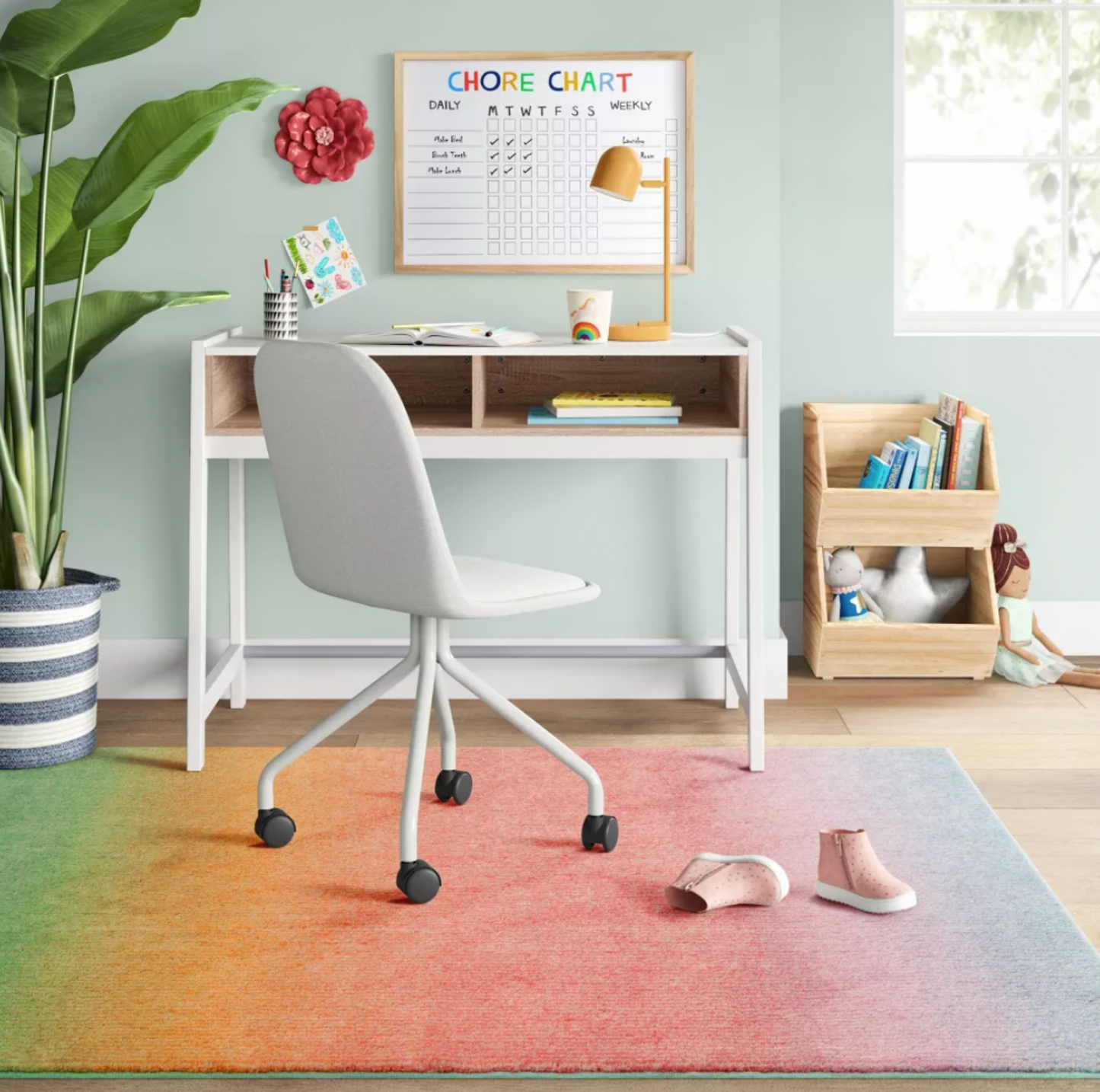 Coin bureau d'enfant avec bureau blanc, chaise, tableau des tâches et tapis touffeté en dégradé arc-en-ciel couvrant le sol avec chaussures et plante