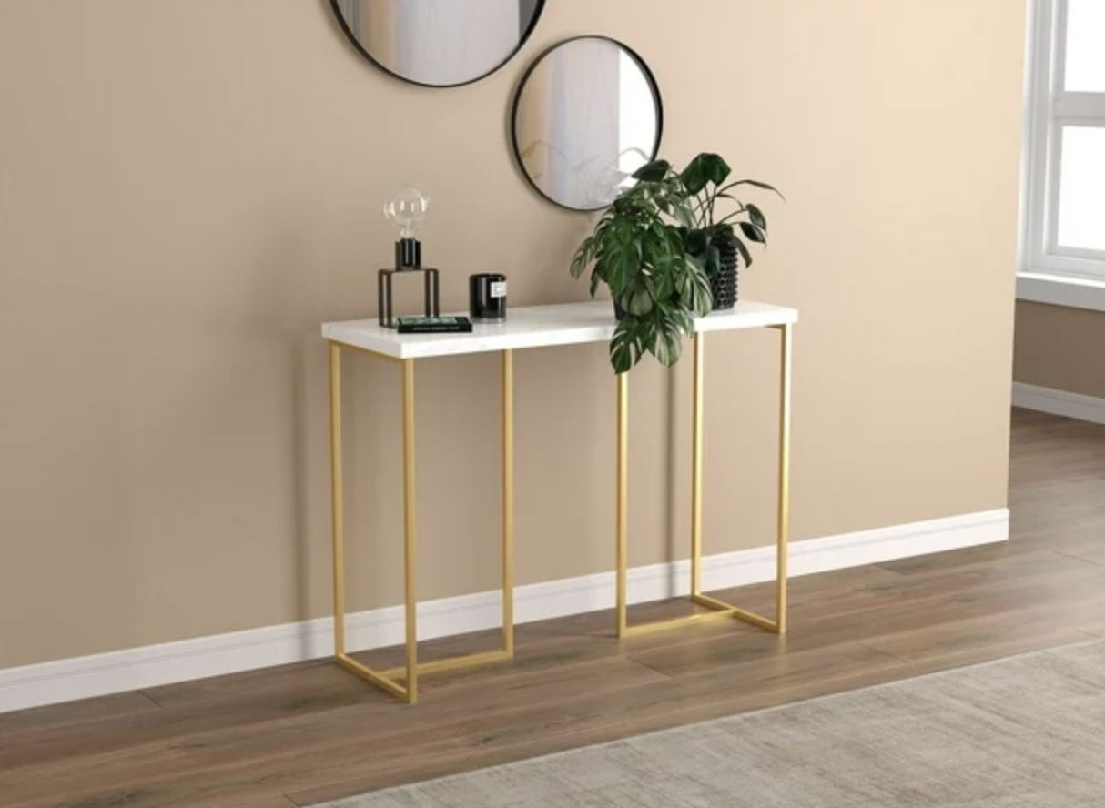 Gros plan de la table console en marbre blanc avec base dorée dans une entrée avec miroirs et plante verte