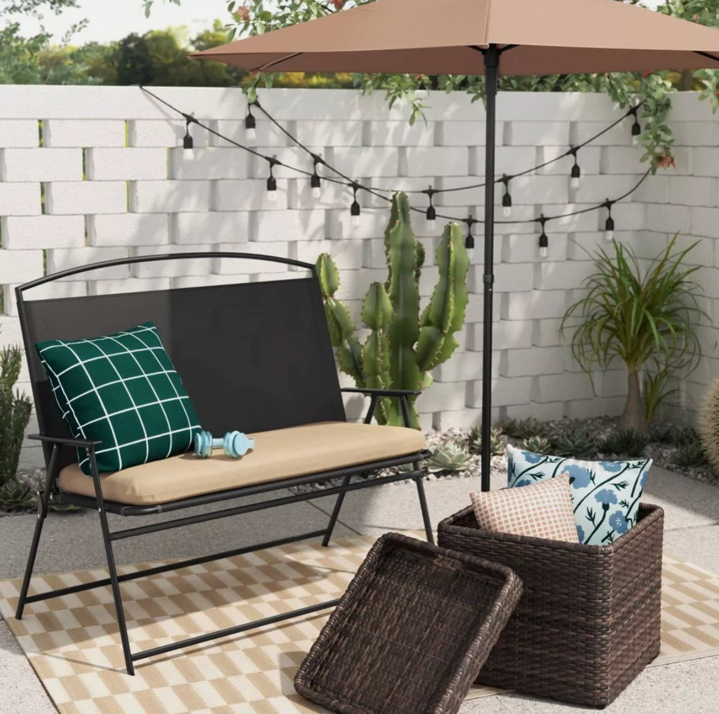 Table de rangement en osier brun avec plateau et coussins à côté d'un banc de patio noir sous parasol beige sur tapis