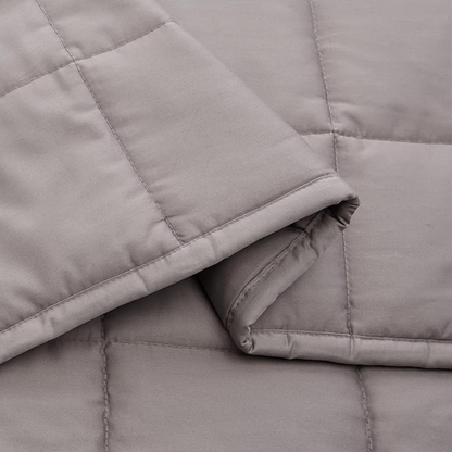 Gros plan d'une couverture lestée grise pliée avec piqûres carrées matelassées et finition coton douce