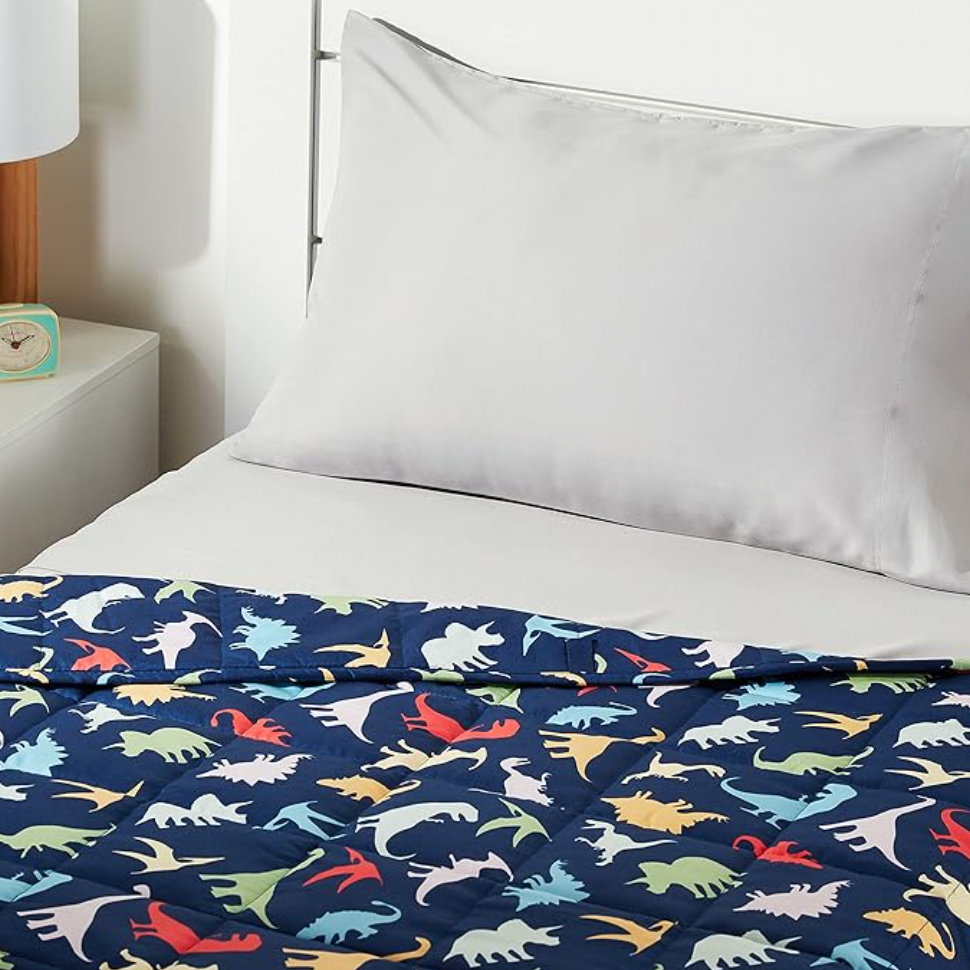 Navy blue dinosaur print weighted blanket on bed with white pillow in kids bedroom