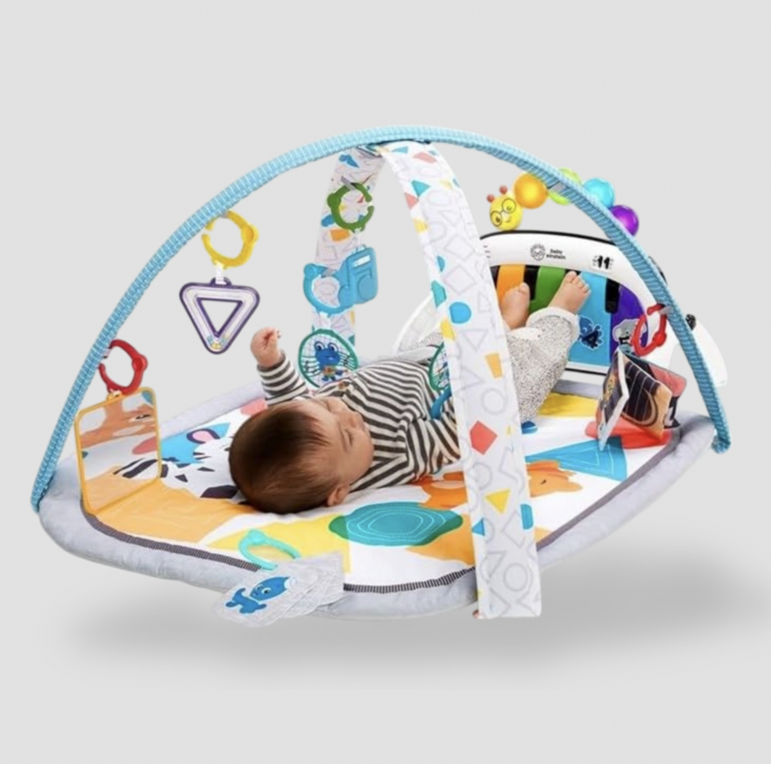 Bébé allongé sur le tapis d'éveil Baby Einstein avec arche turquoise, jouets suspendus et panneau piano amovible en pyjama à rayures