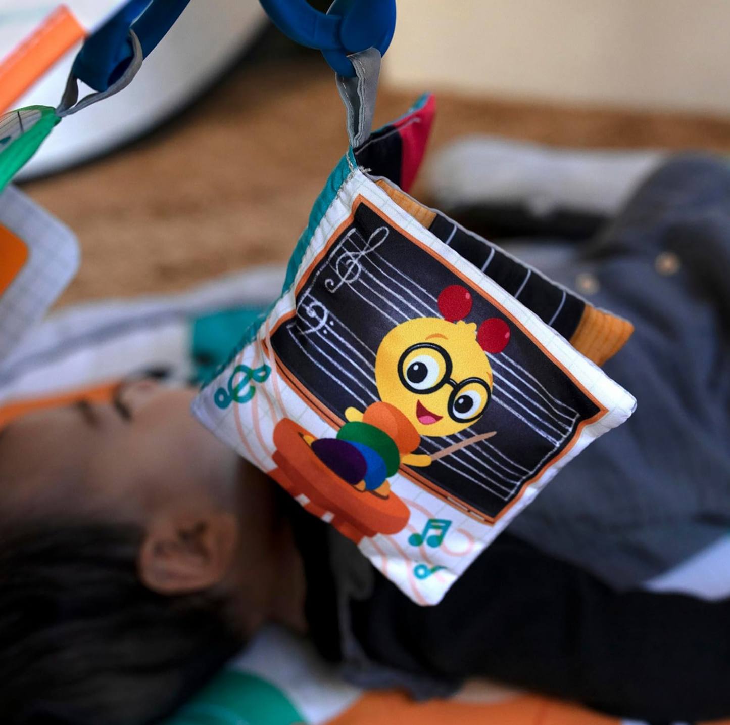 Gros plan du livre en tissu froissant suspendu à l'arche du tapis d'éveil avec illustration de partition musicale et chenille de dessin animé