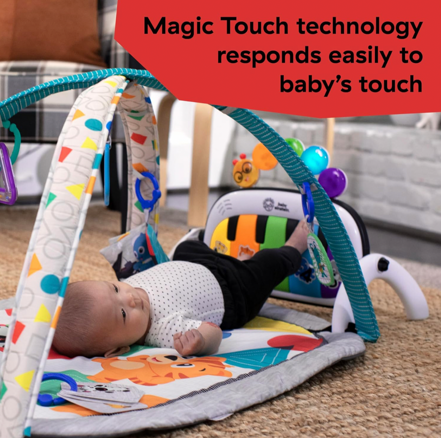 Bébé sur le dos donnant des coups de pieds sur le piano amovible Baby Einstein sur l'arche turquoise du tapis d'éveil, mention Magic Touch technology