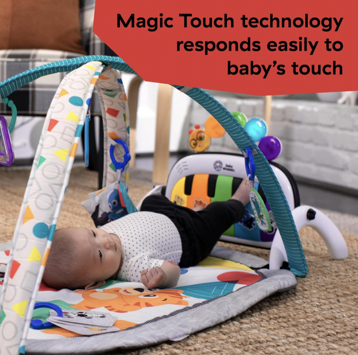 Bébé sur le dos donnant des coups de pieds sur le piano amovible Baby Einstein sur l'arche turquoise du tapis d'éveil, mention Magic Touch technology
