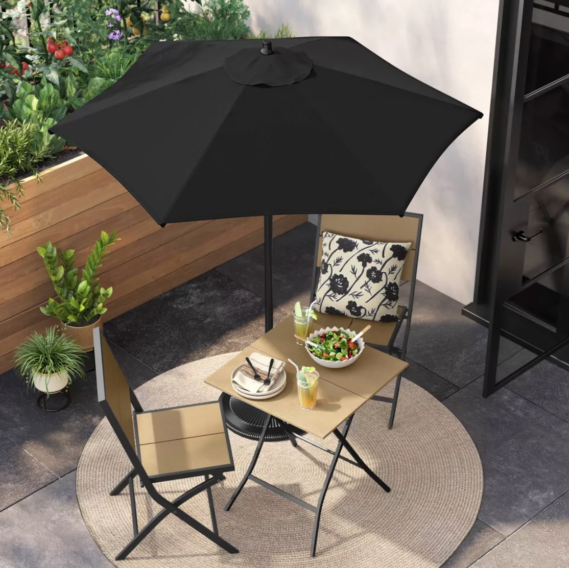 Parasol de patio noir au-dessus d'une table bistro avec saladier et plants de tomates sur terrasse