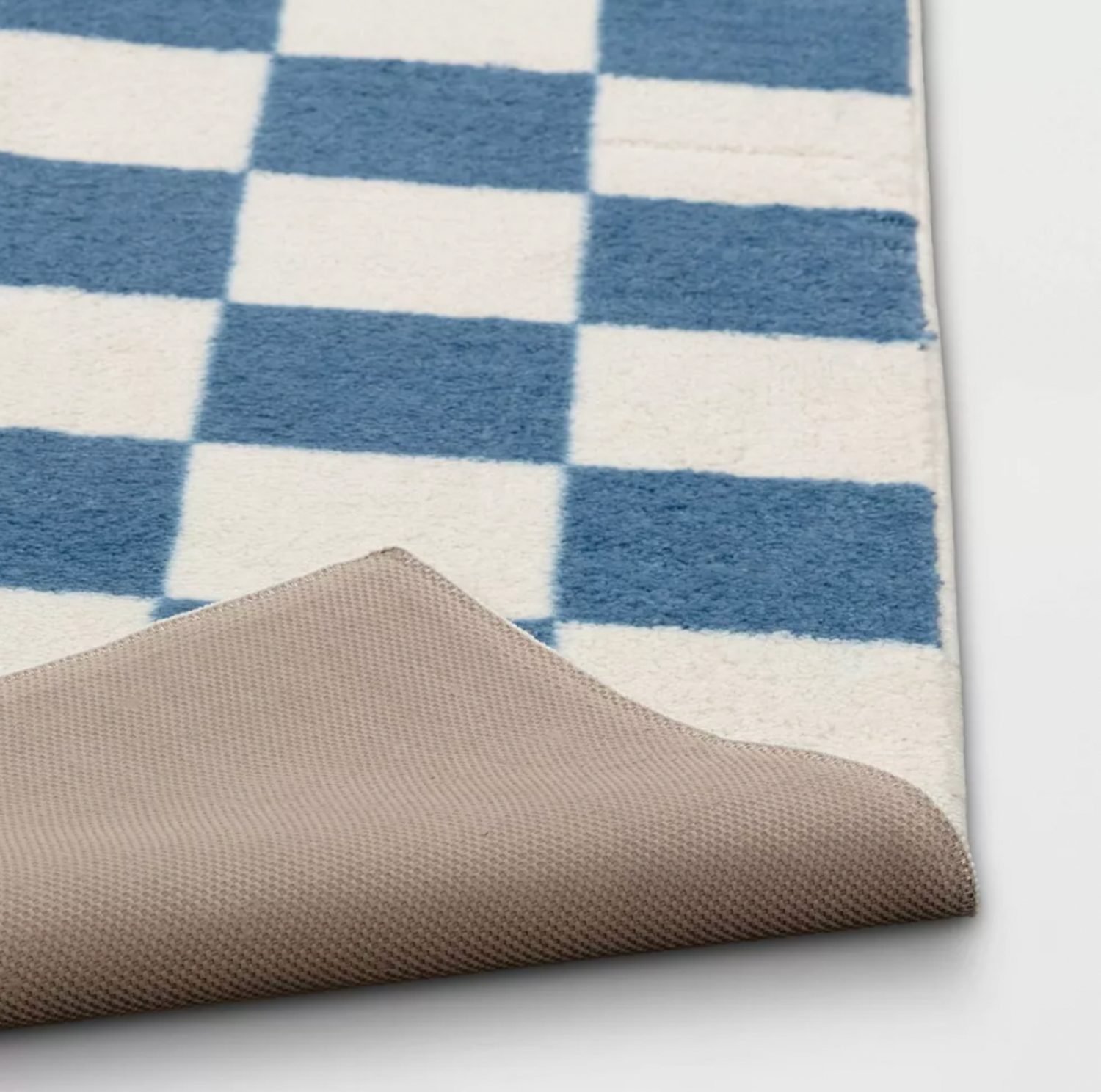 Coin du tapis pour enfants à damier bleu replié pour montrer le dessous antidérapant beige
