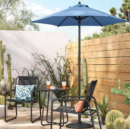 Parasol de patio bleu dans une scène extérieure désertique avec table bistro, chaises et cactus en pot