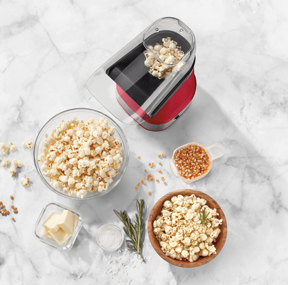 Vue de dessus de la machine à popcorn Cuisinart rouge avec maïs soufflé, grains, beurre et romarin sur comptoir en marbre