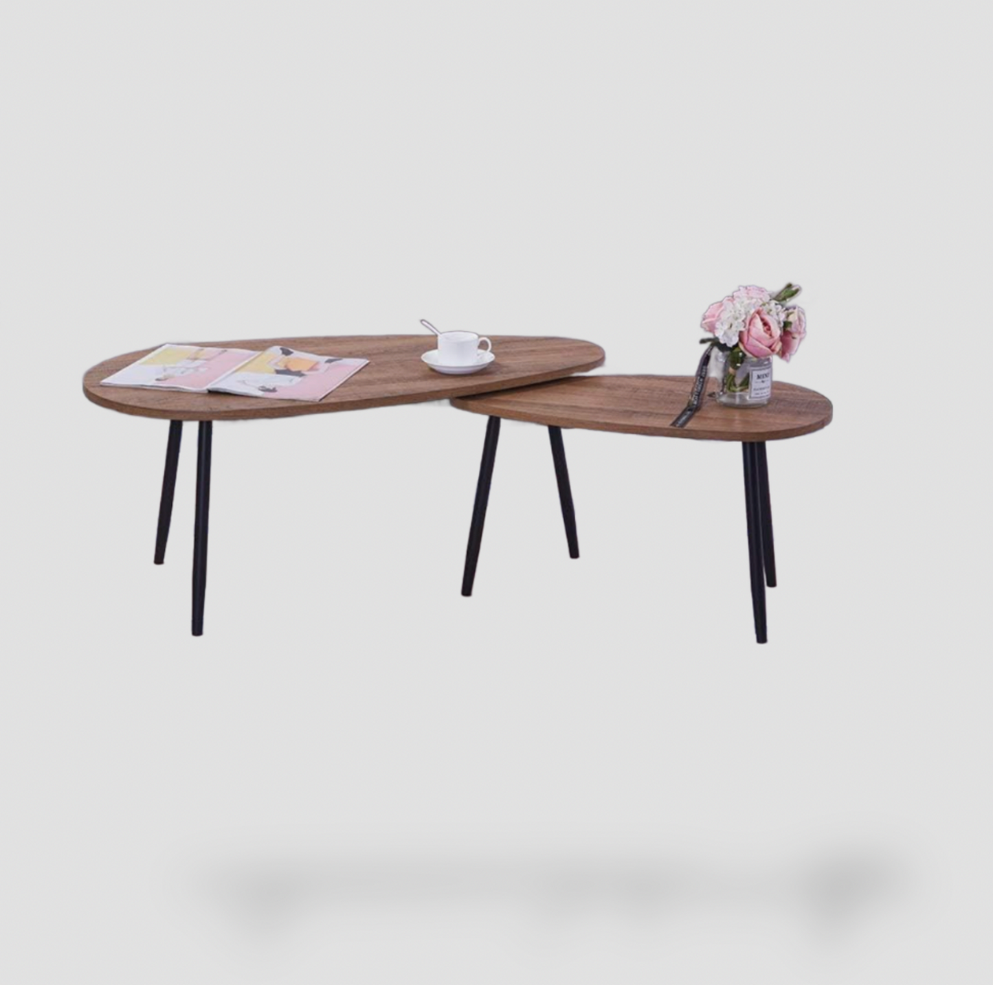 Ensemble de 2 tables basses gigognes ovales avec plateaux effet bois noyer et pieds métalliques noirs fuselés stylisés avec magazine, tasse et roses roses