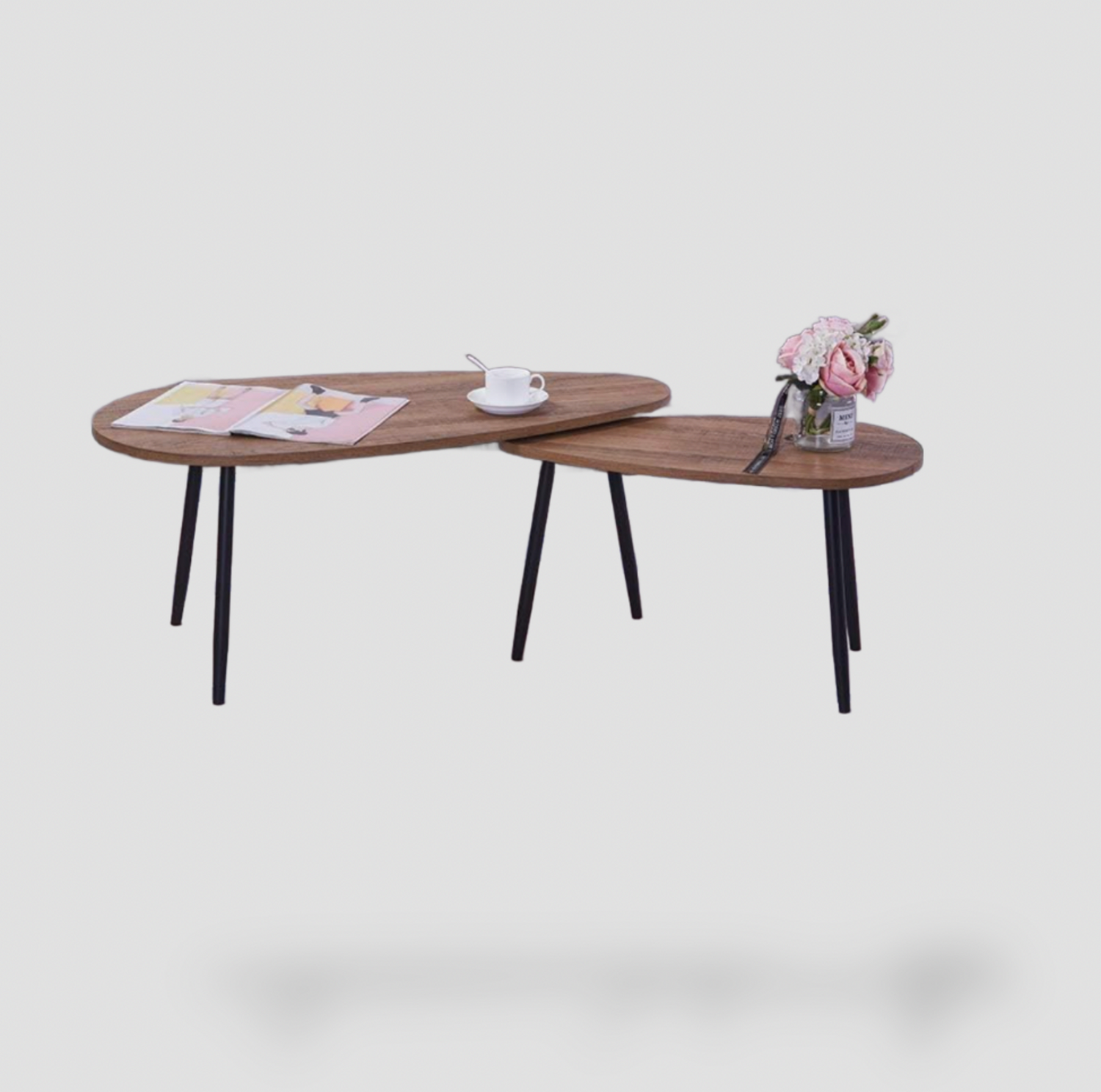 Ensemble de 2 tables basses gigognes ovales avec plateaux effet bois noyer et pieds métalliques noirs fuselés stylisés avec magazine, tasse et roses roses