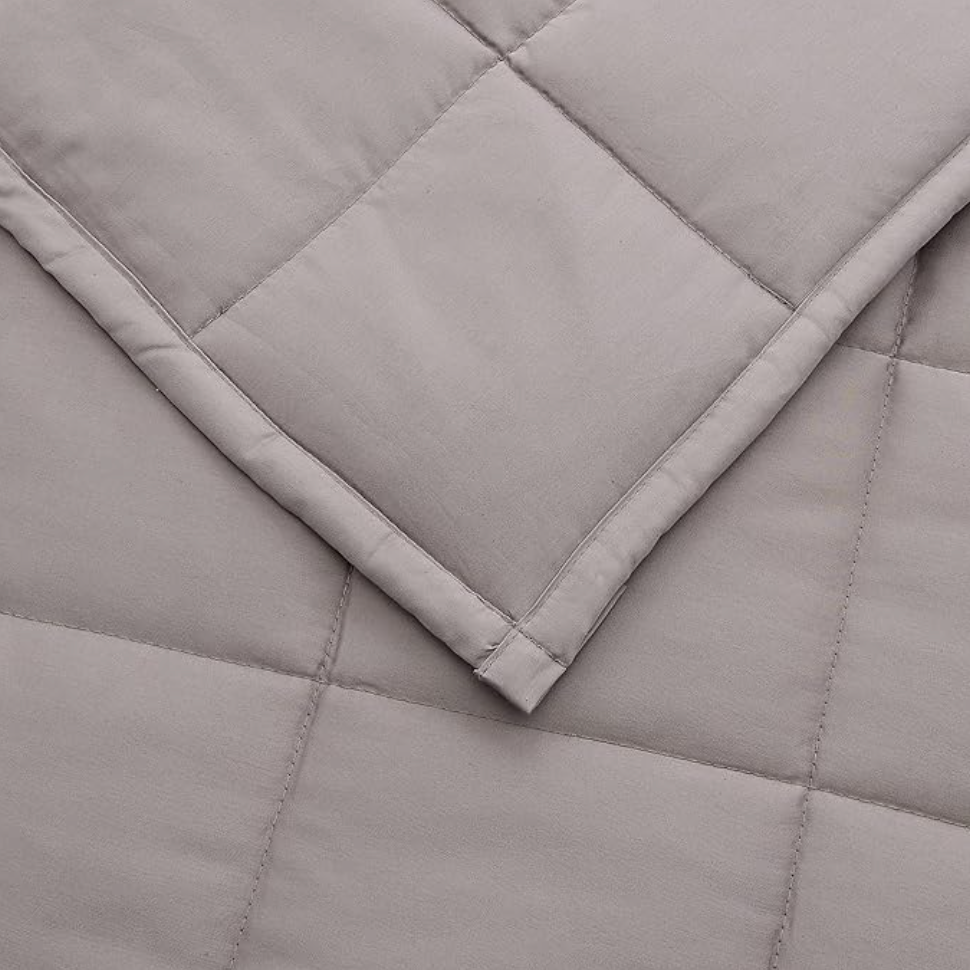 Gros plan d'un coin de couverture lestée matelassée grise avec piqûres carrées et ourlet replié