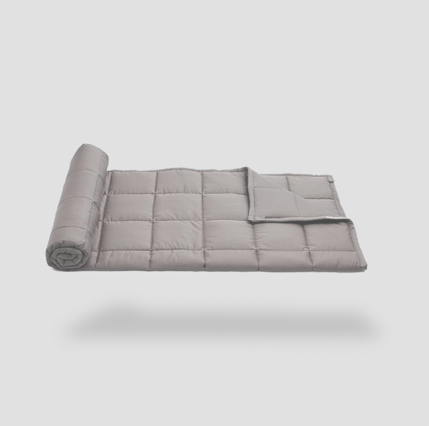 Couverture lestée grise matelassée à demi enroulée sur fond blanc, vue de côté