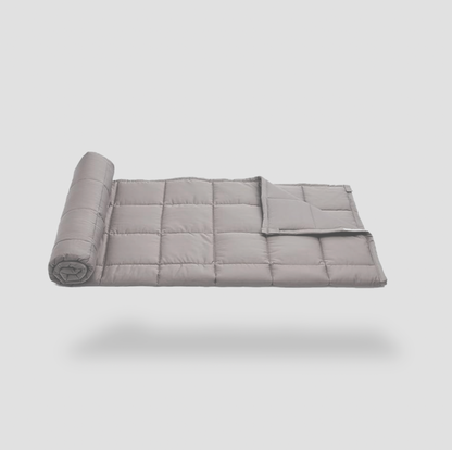 Couverture lestée grise matelassée à demi enroulée sur fond blanc, vue de côté