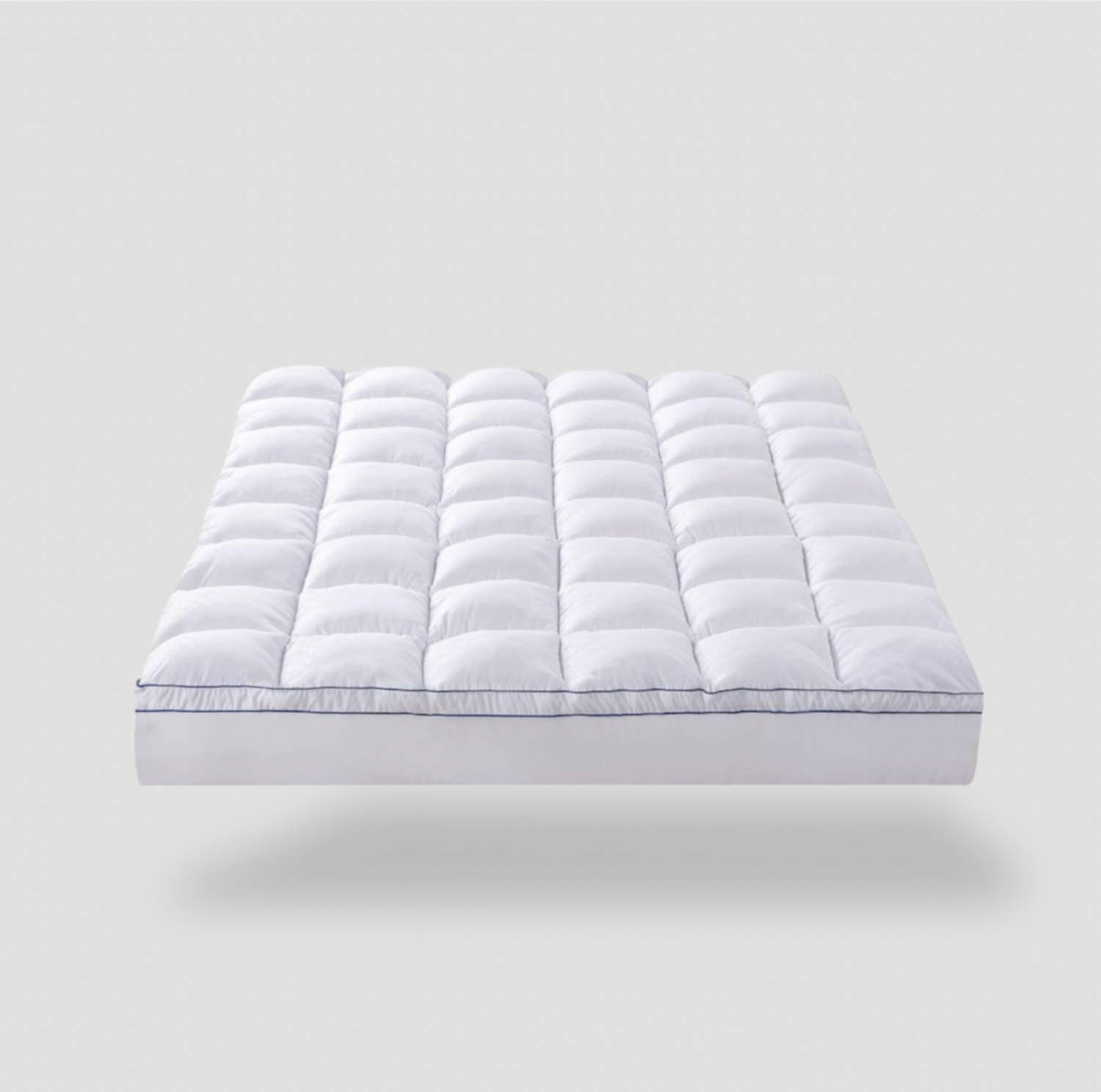 Surmatelas grand simple matelassé blanc avec motif quadrillé et passepoil marine, vue trois-quarts sur fond gris