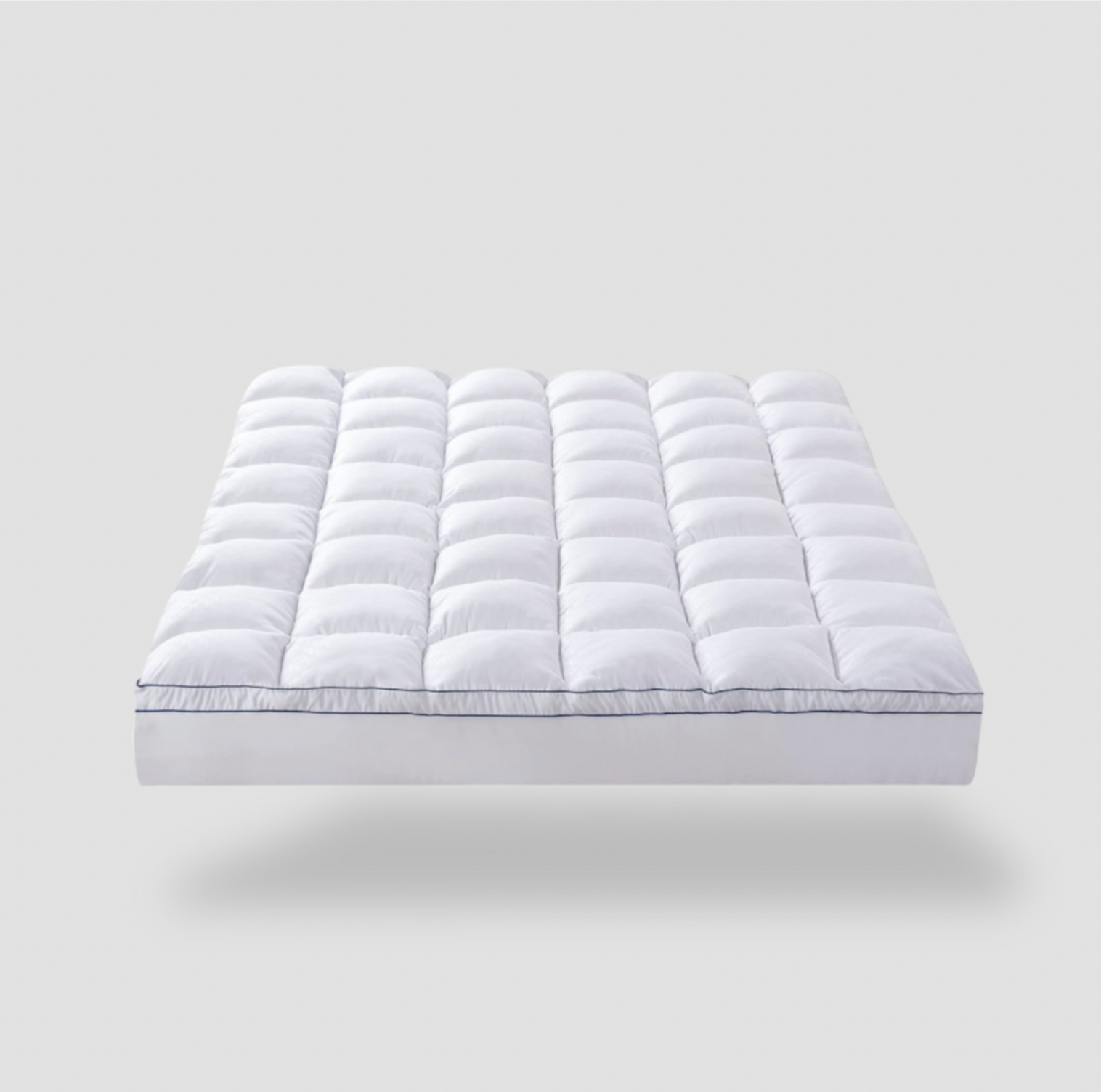 Surmatelas grand simple matelassé blanc avec motif quadrillé et passepoil marine, vue trois-quarts sur fond gris