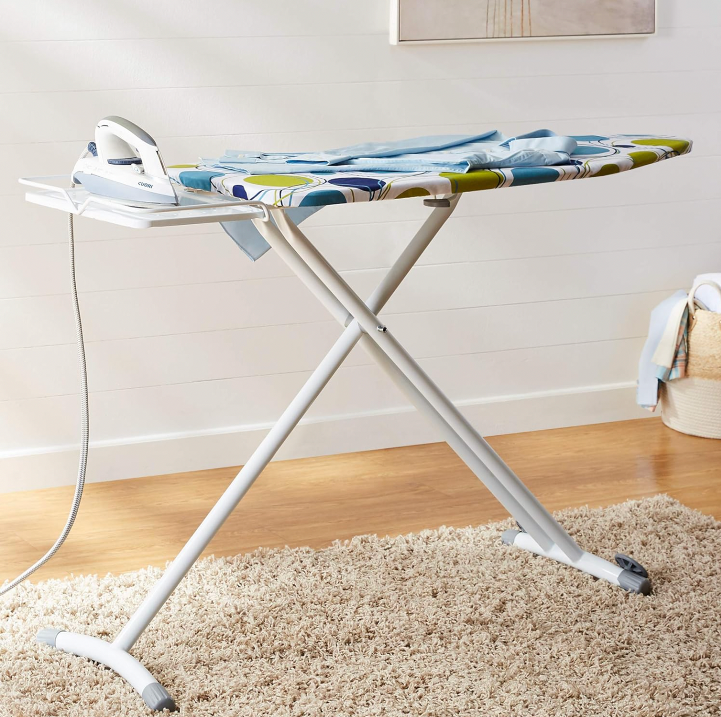 Ironing board with circles print cover, iron resting on rest and folded blue shirt in laundry room with shiplap wall