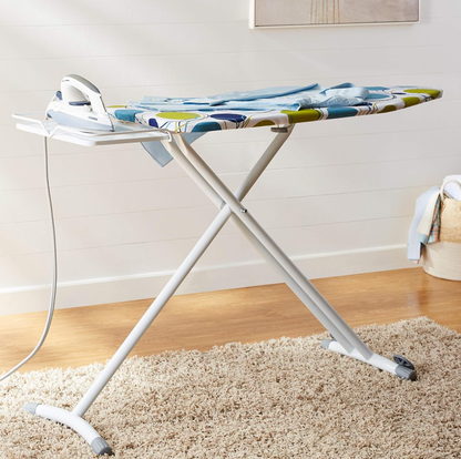 Ironing board with circles print cover, iron resting on rest and folded blue shirt in laundry room with shiplap wall