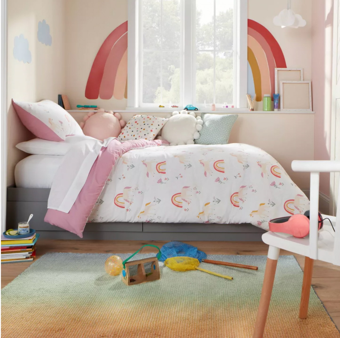 Chambre d'enfant avec décalques d'arc-en-ciel au mur, literie imprimée licornes et tapis en dégradé vert sur plancher de bois