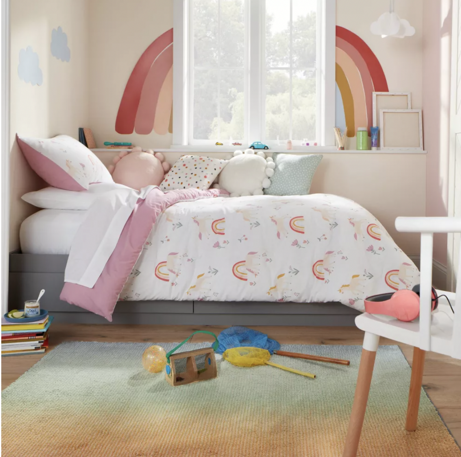 Chambre d'enfant avec décalques d'arc-en-ciel au mur, literie imprimée licornes et tapis en dégradé vert sur plancher de bois