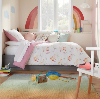 Chambre d'enfant avec décalques d'arc-en-ciel au mur, literie imprimée licornes et tapis en dégradé vert sur plancher de bois