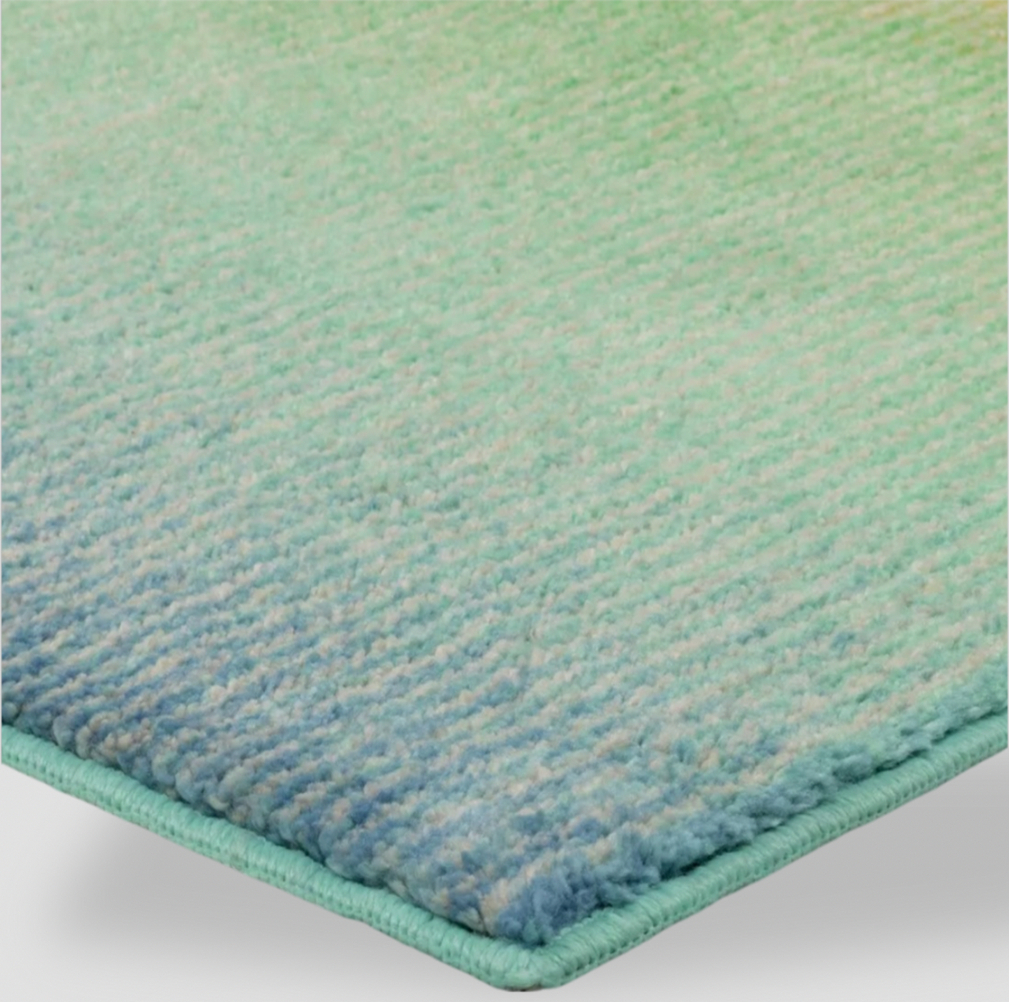 Gros plan d'un coin du tapis bordé avec poil touffeté vert vers bleu et bordure surfilée assortie