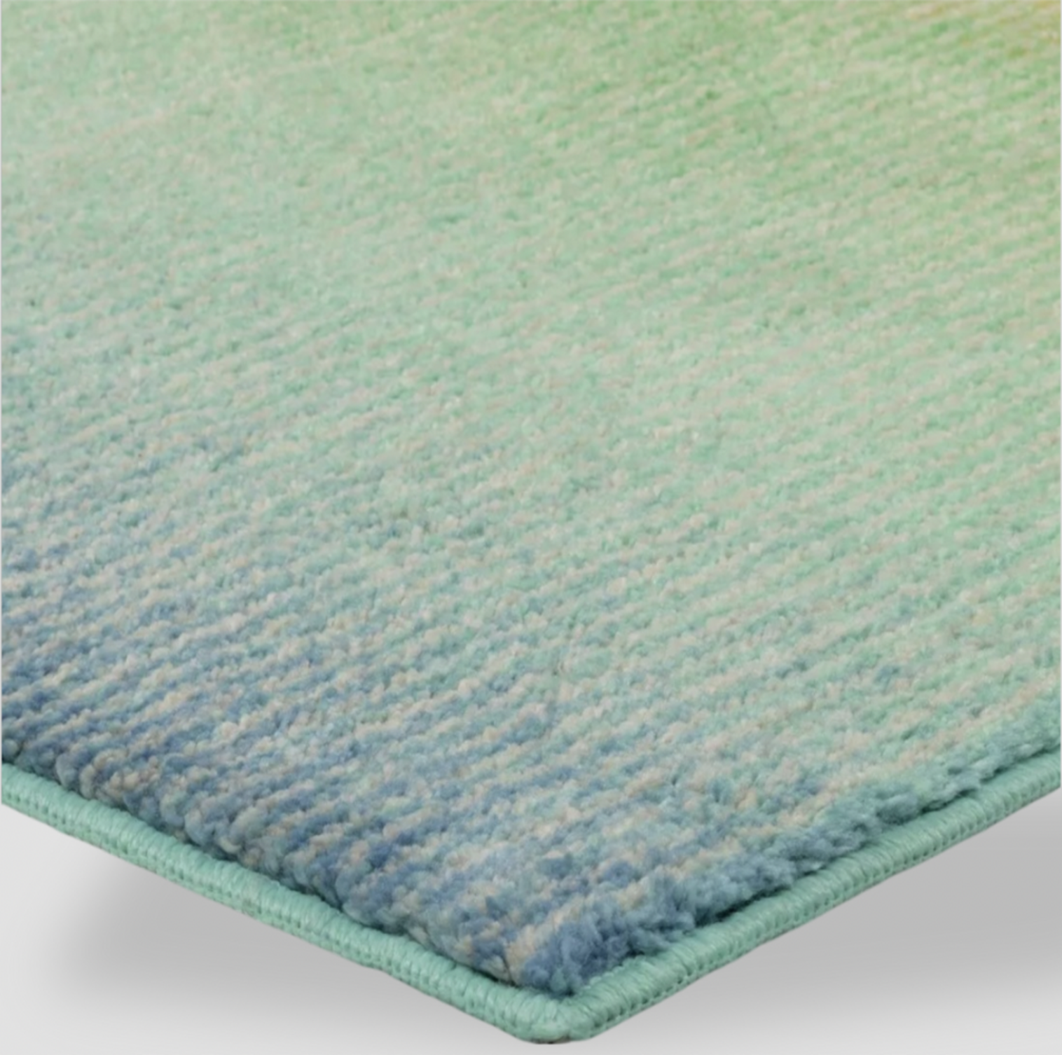 Gros plan d'un coin du tapis bordé avec poil touffeté vert vers bleu et bordure surfilée assortie
