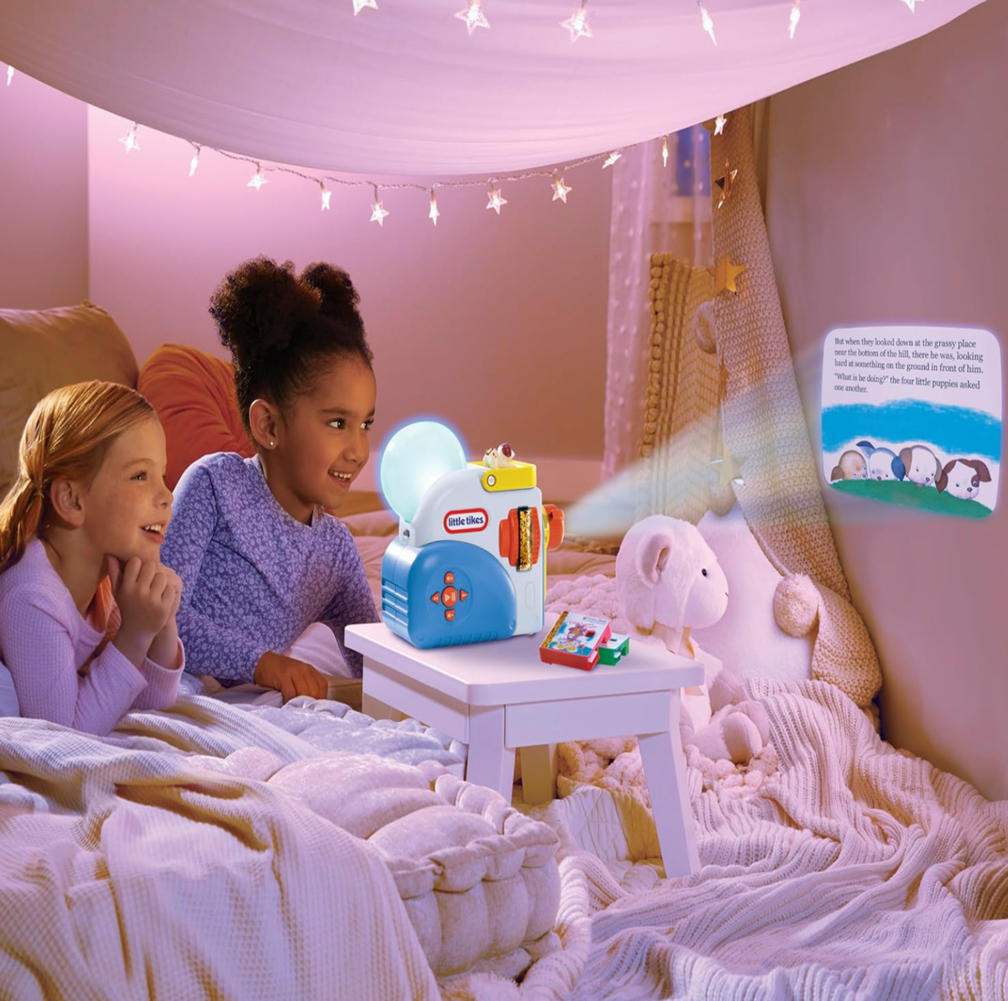 Deux fillettes regardant une histoire projetée par la Little Tikes Story Dream Machine dans une tente de chambre éclairée de guirlandes