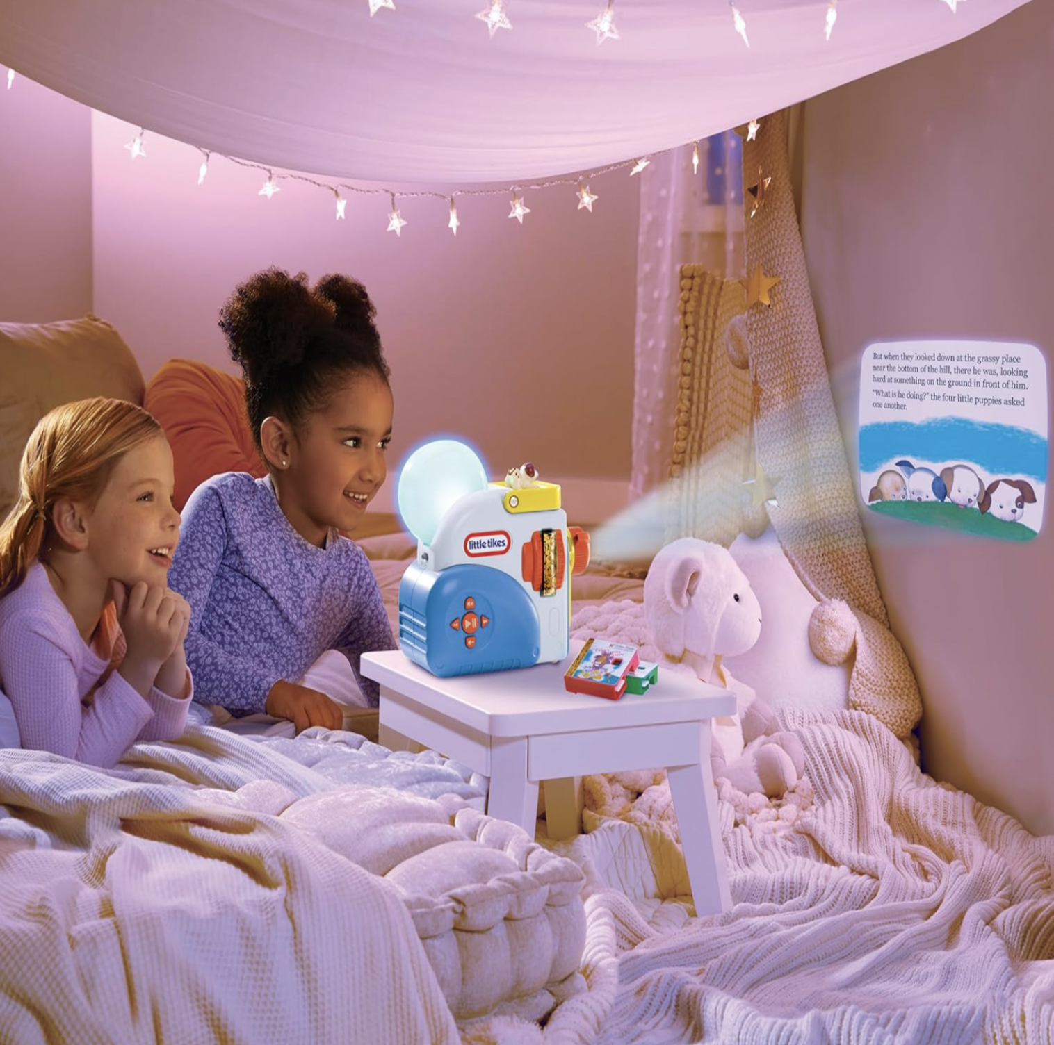 Deux fillettes regardant une histoire projetée par la Little Tikes Story Dream Machine dans une tente de chambre éclairée de guirlandes