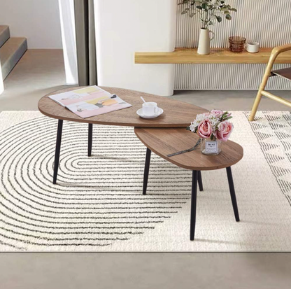 Paire de tables gigognes ovales avec plateaux noyer et pieds noirs fuselés dans un salon sur tapis crème à motif courbe avec buffet et chaise à manger derrière