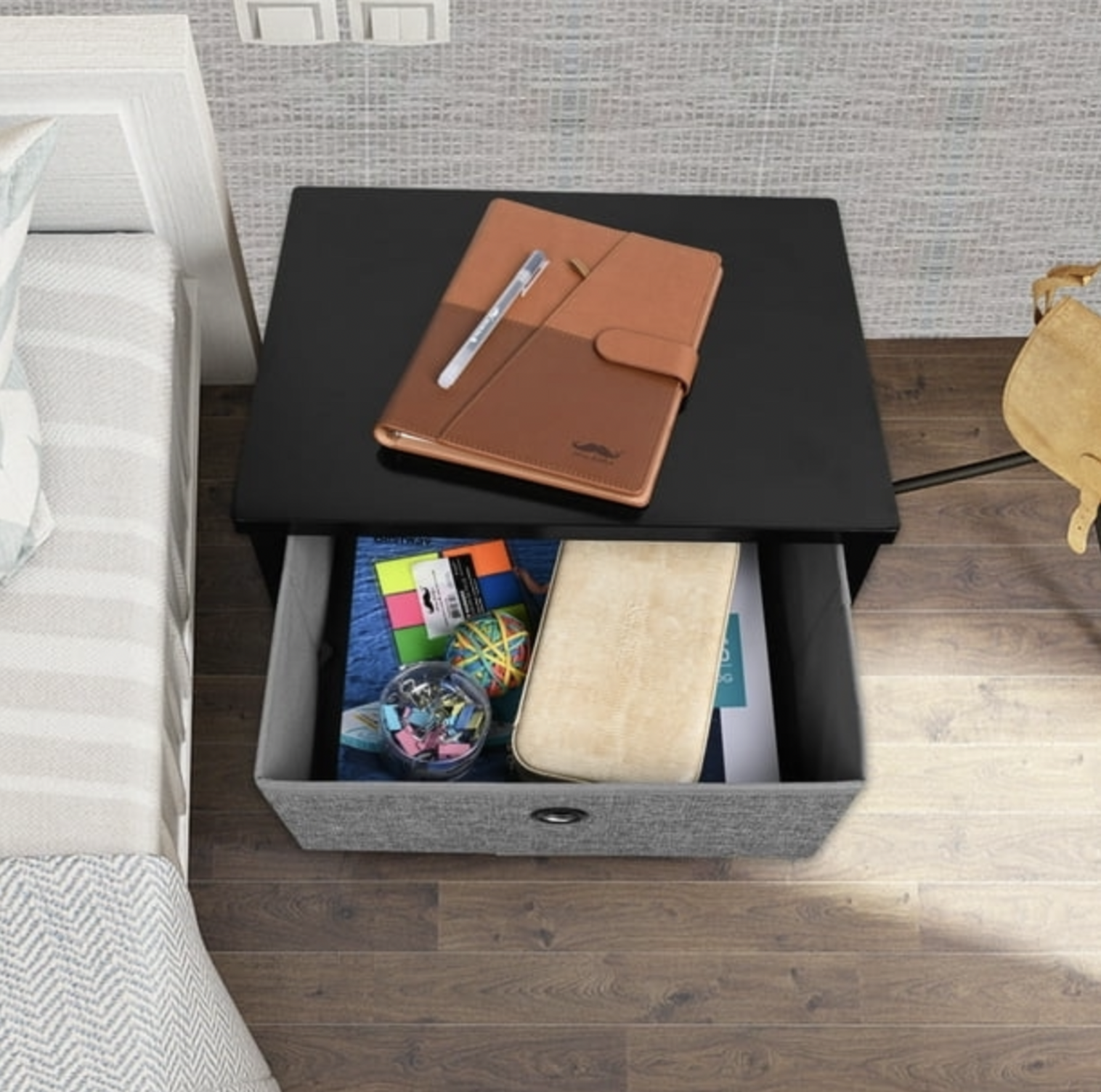 Vue plongeante du dessus de la table de chevet noire avec carnet en cuir à côté du tiroir en tissu gris ouvert contenant de la papeterie
