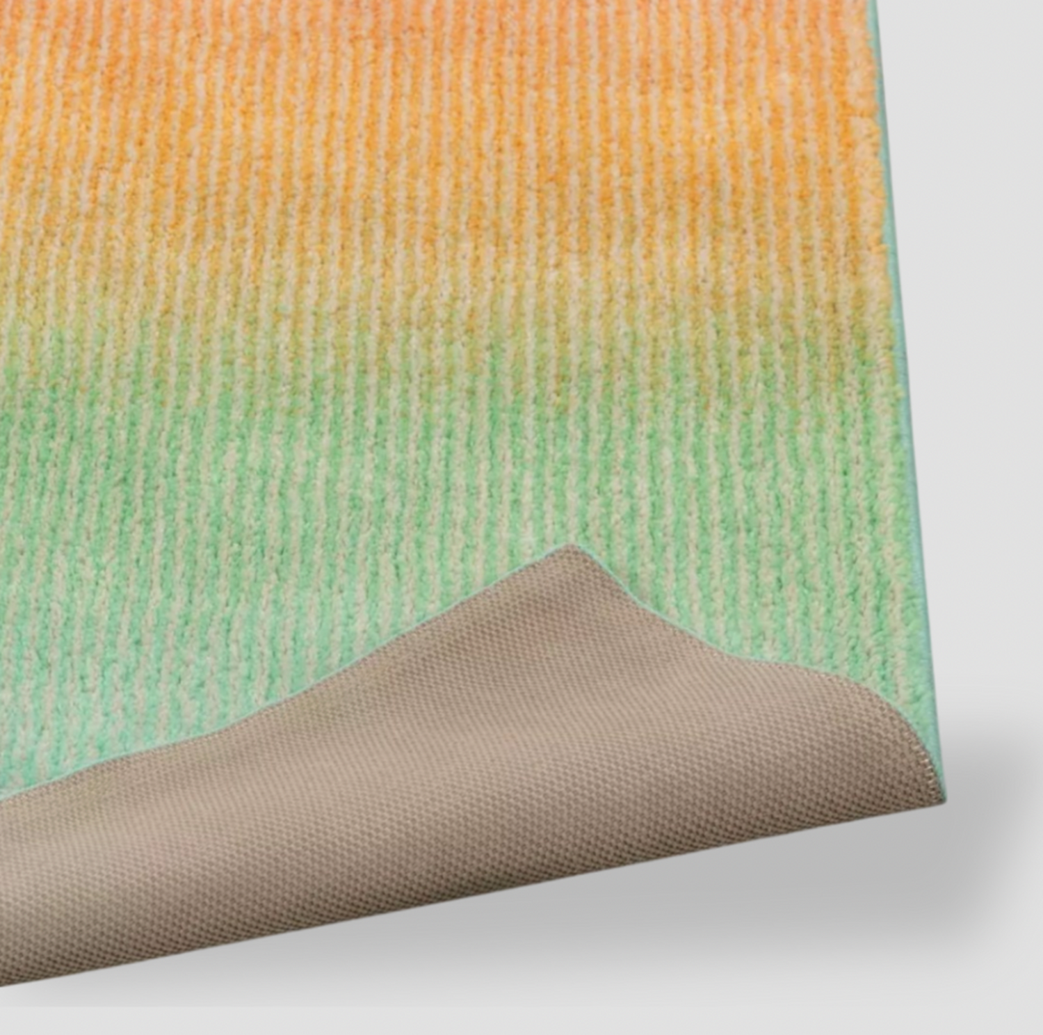 Détail du coin replié du tapis pour enfants en dégradé arc-en-ciel montrant la surface touffetée orange à vert et l'envers antidérapant beige