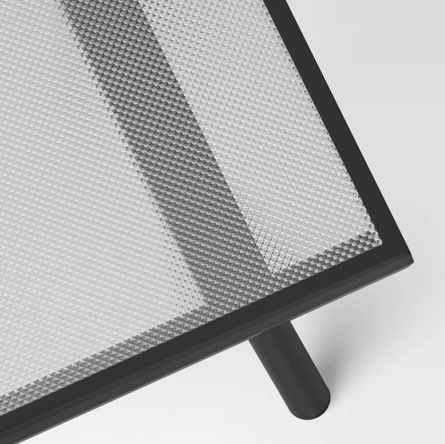Gros plan du coin du plateau en verre texturé avec cadre métallique noir et pied incliné