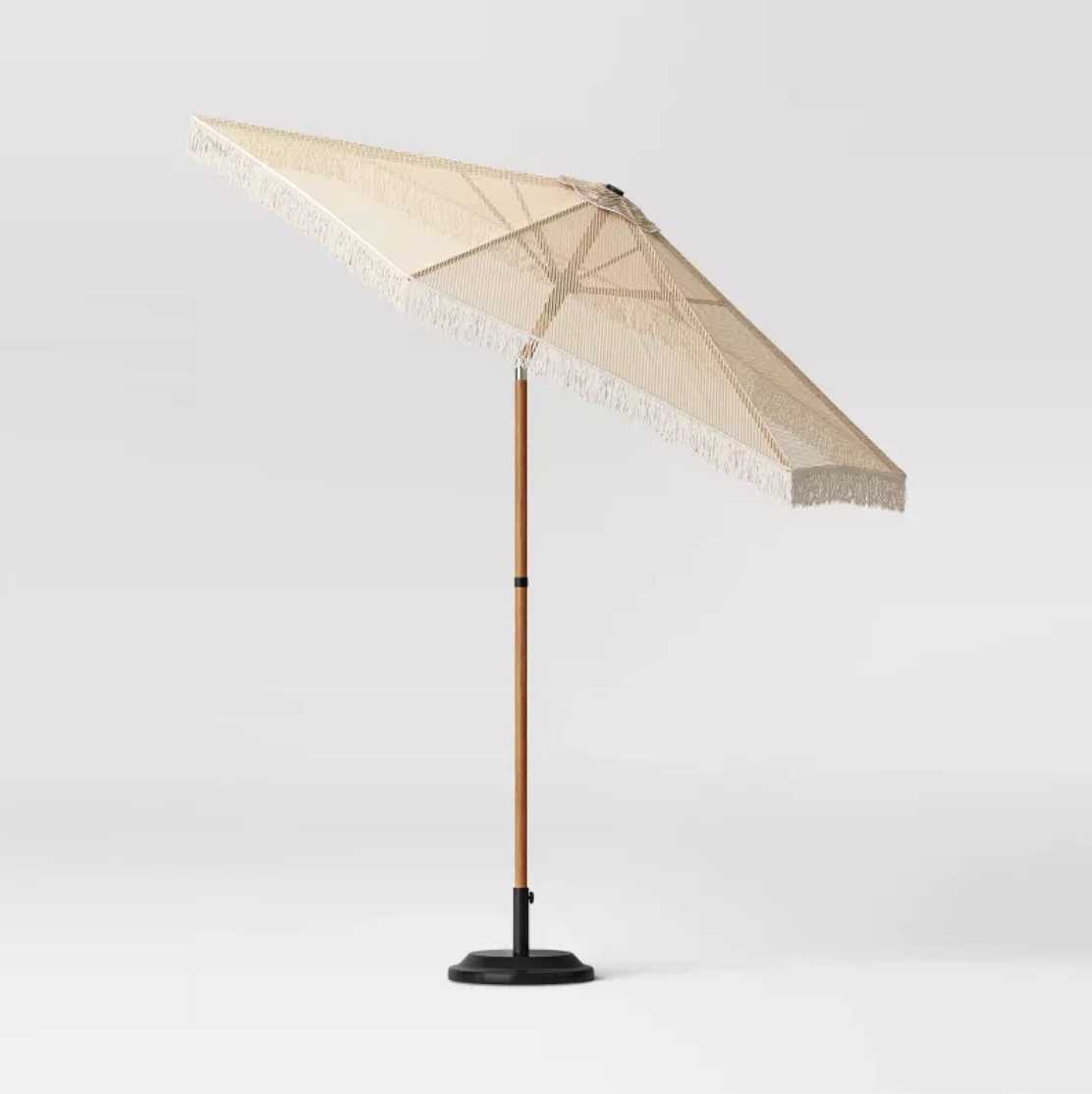 Parasol de patio en macramé beige incliné sur mât en faux bois avec base lestée noire, vue de côté