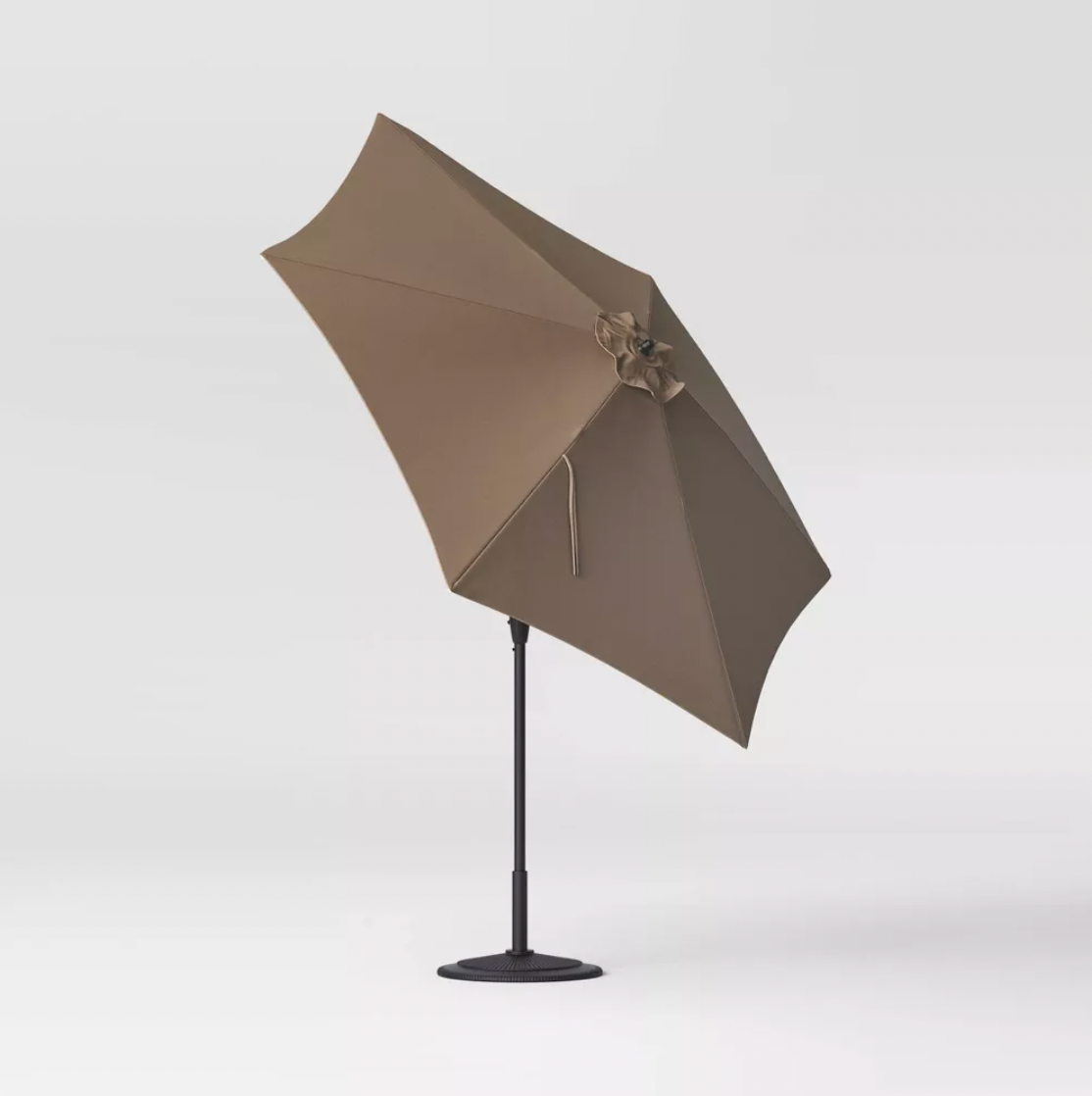 Tilted 9 foot brown patio umbrella on black pole with weighted base, side view