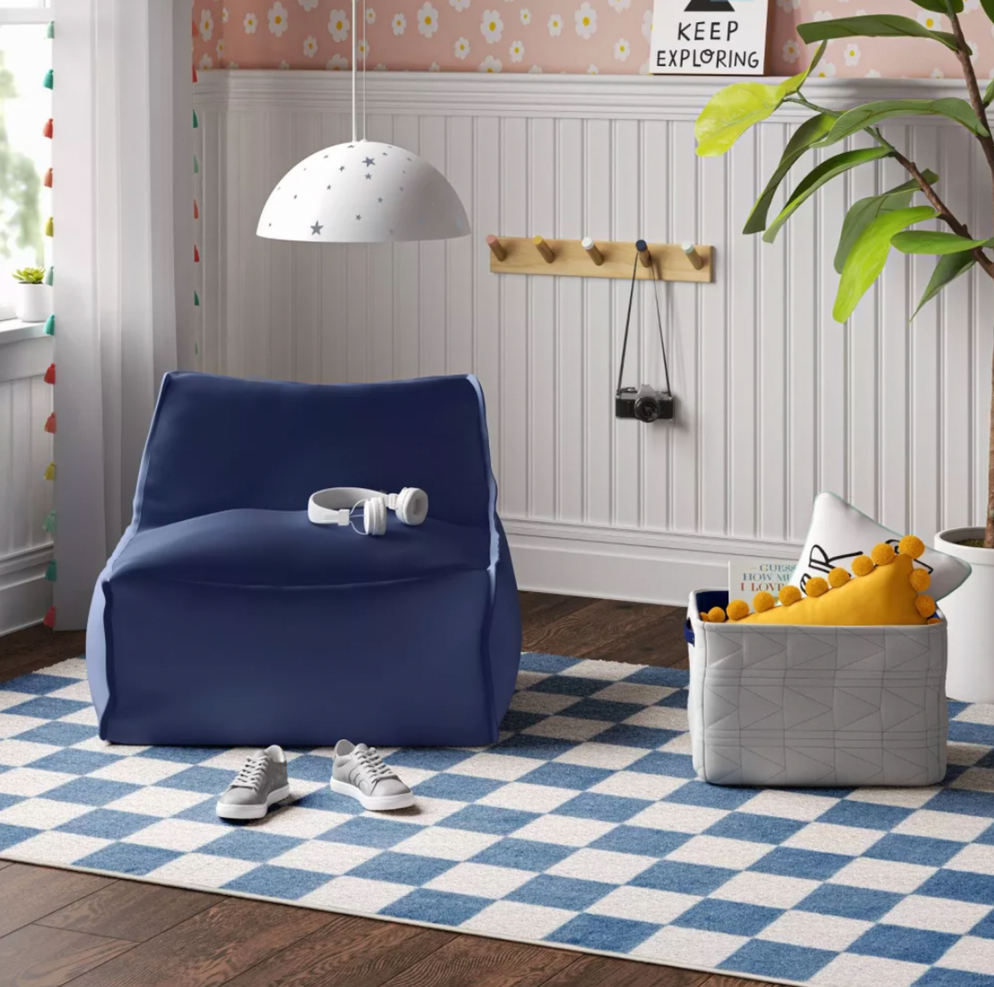 Tapis pour enfants à damier bleu dans une salle de jeux avec pouf bleu marine, écouteurs blancs et espadrilles