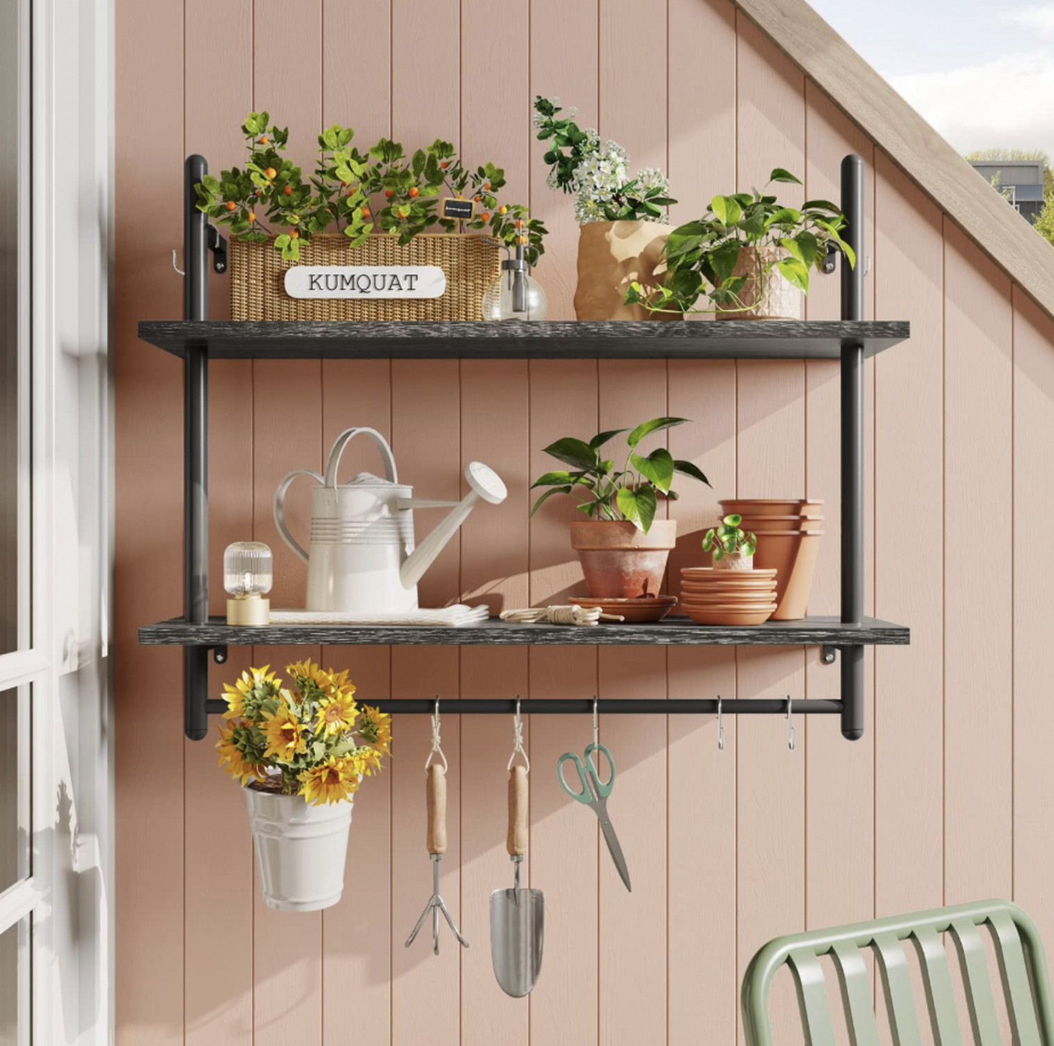 Étagère à tuyaux noire à deux étages sur un mur rose à planches de bois avec plantes en pot et arrosoir blanc dans une véranda