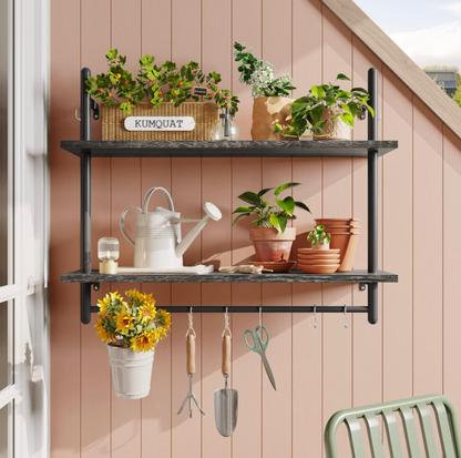 Étagère à tuyaux noire à deux étages sur un mur rose à planches de bois avec plantes en pot et arrosoir blanc dans une véranda