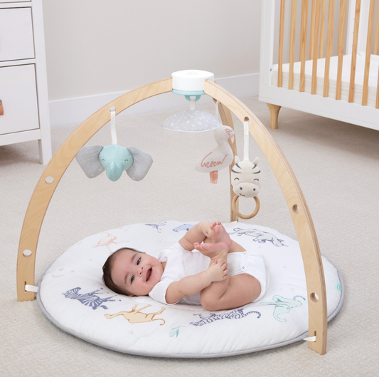 Baby playing on Rising Star round safari-print activity gym with wooden arches, elephant, zebra and projector toys