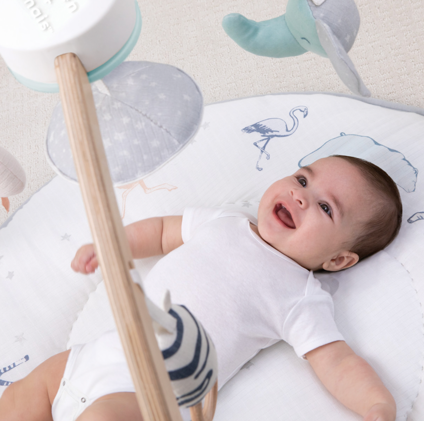 Bébé souriant allongé sous l'arche en bois Rising Star avec peluches baleine et zèbre suspendues
