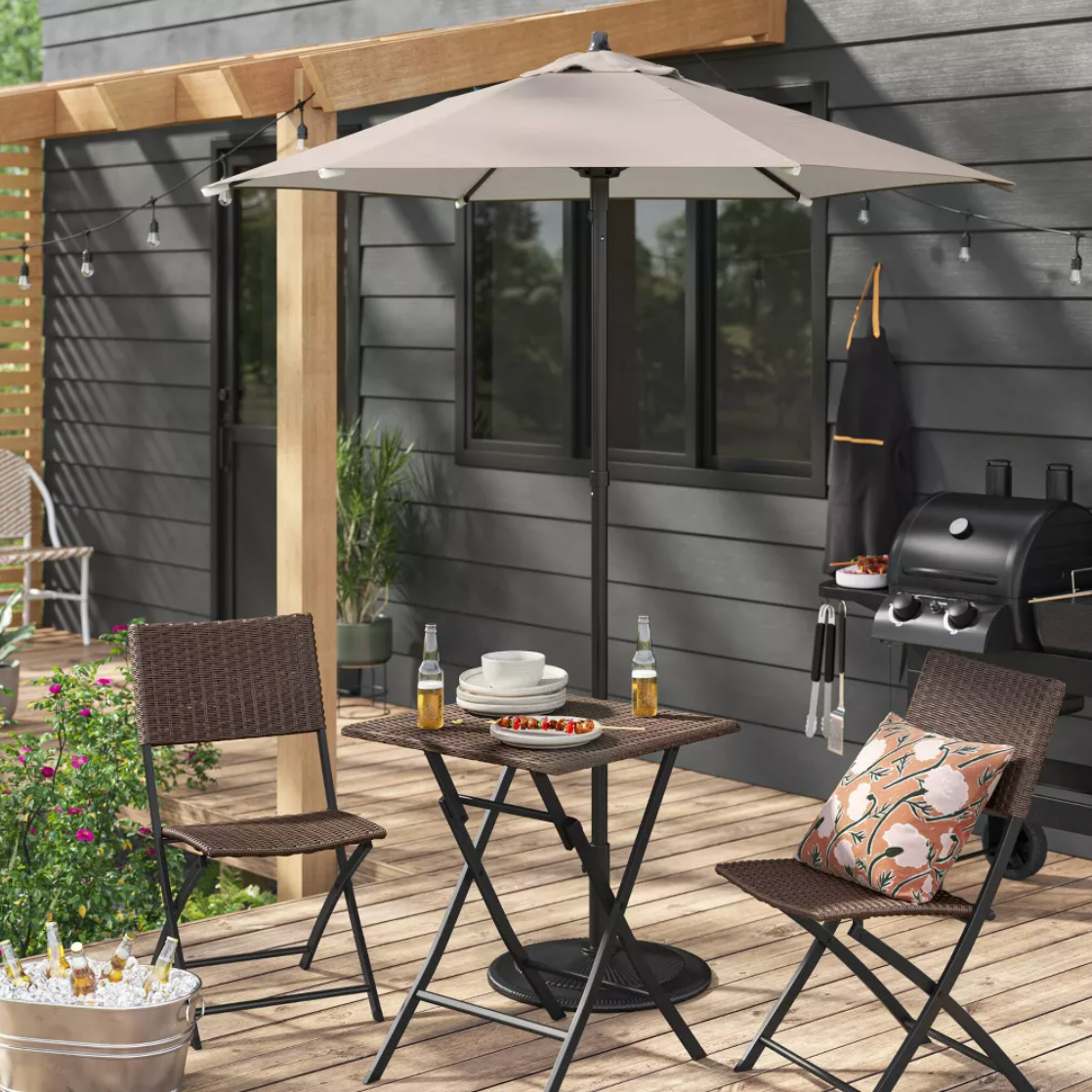 Parasol de patio taupe sur terrasse en bois avec chaises en rotin et gril d'extérieur, vue lifestyle