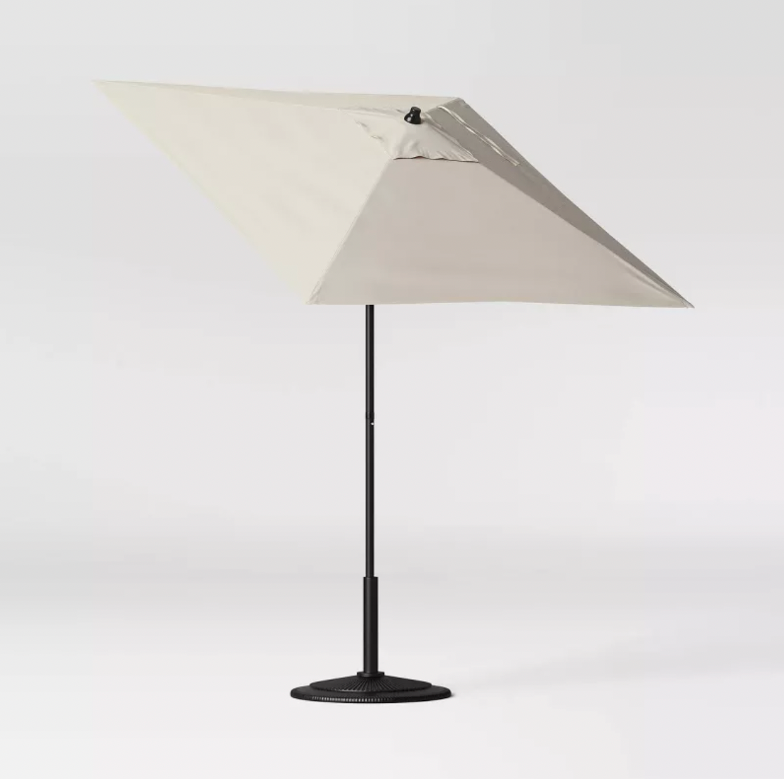 Parasol de patio carré beige incliné sur mât noir avec socle lesté, vue trois-quarts