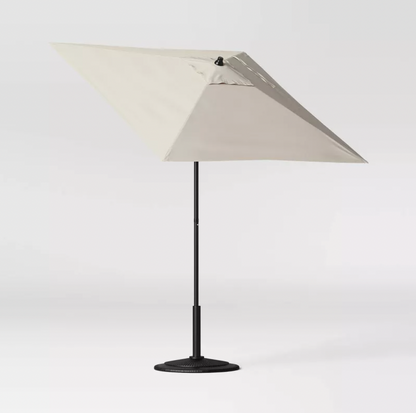 Parasol de patio carré beige incliné sur mât noir avec socle lesté, vue trois-quarts