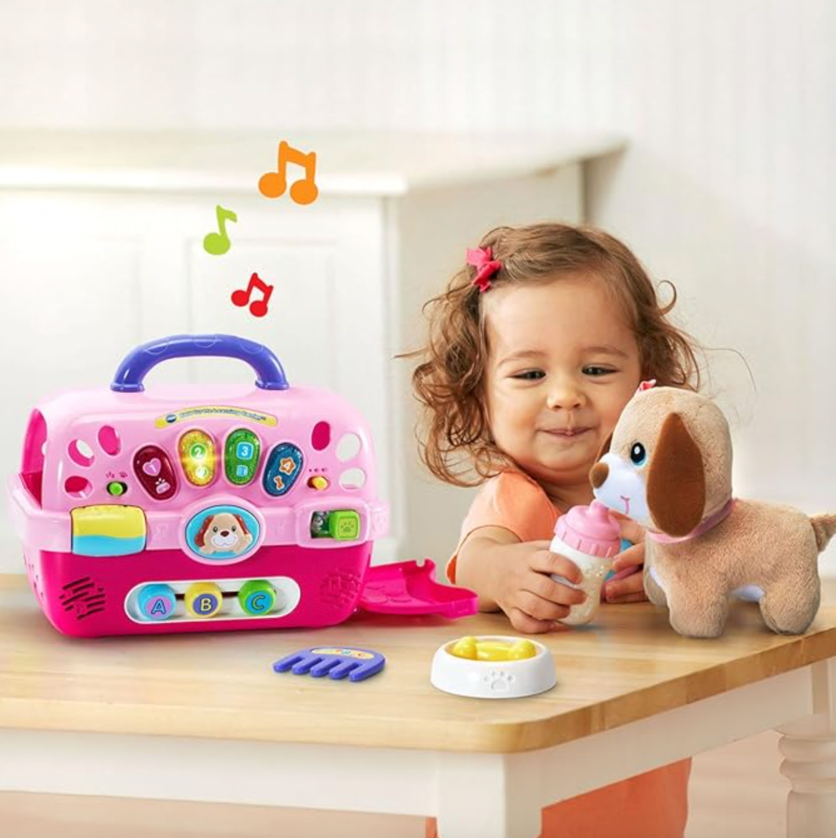 Petite fille jouant avec le jouet de transport éducatif rose VTech et la peluche chiot à une table blanche