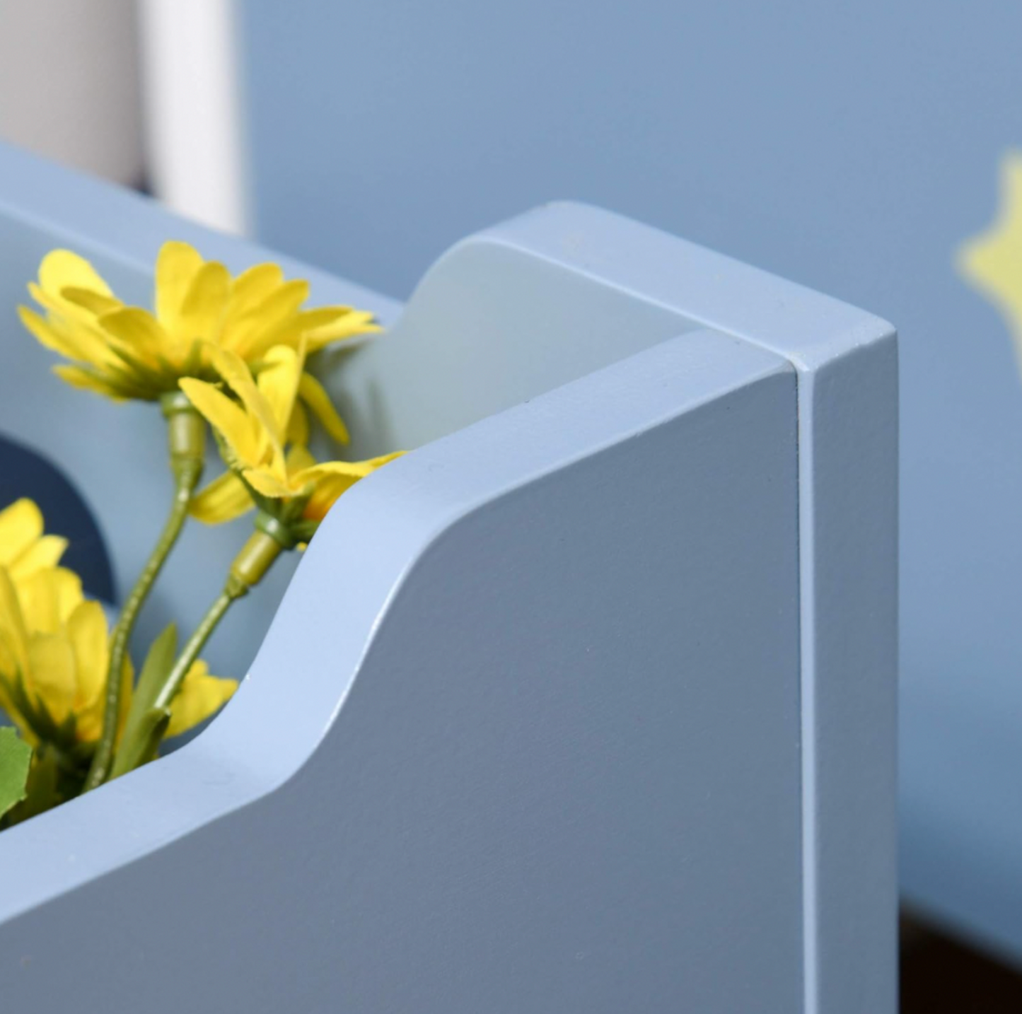 Gros plan de la poignée découpée sur le côté du coffre à jouets en bois bleu avec marguerites jaunes à l'intérieur