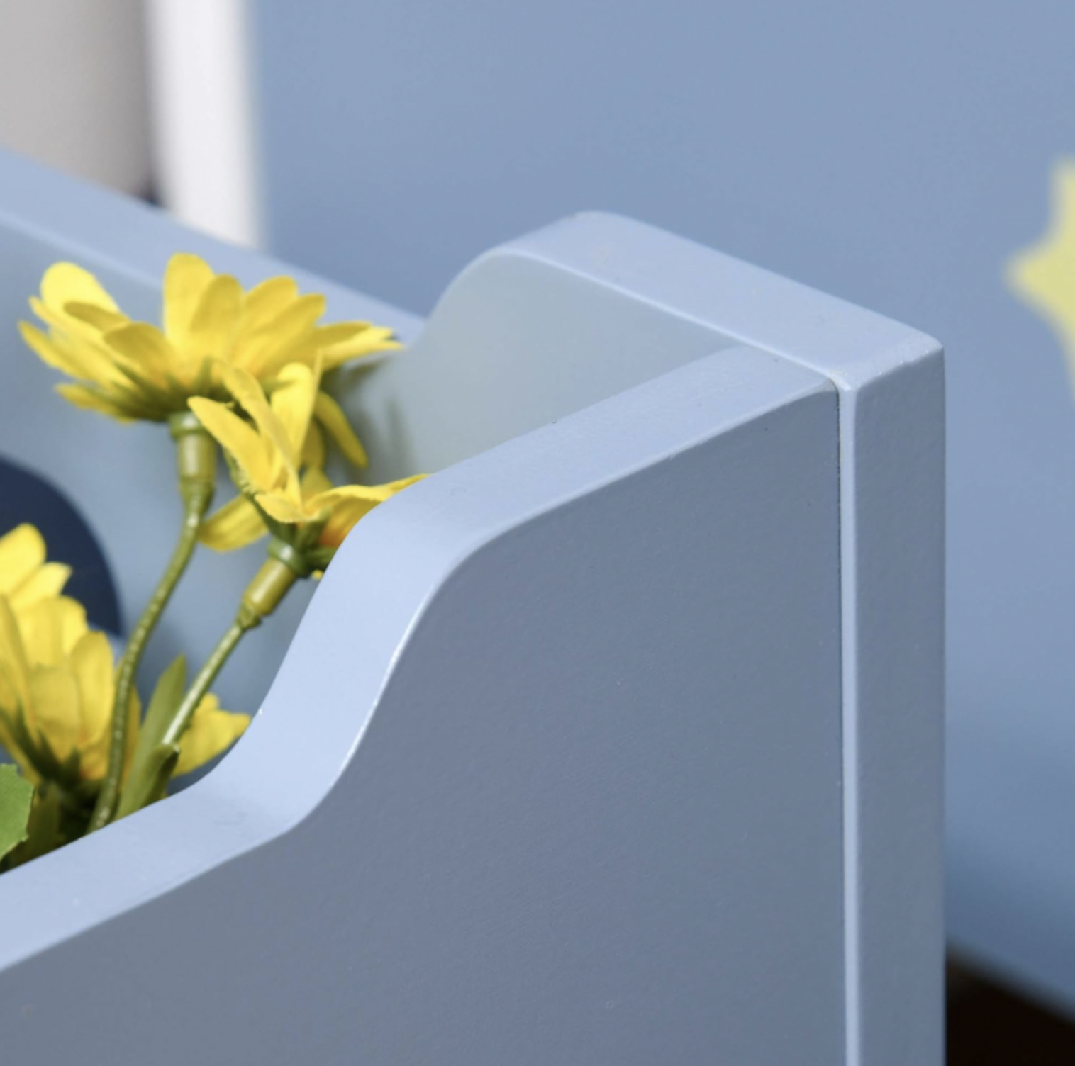 Gros plan de la poignée découpée sur le côté du coffre à jouets en bois bleu avec marguerites jaunes à l'intérieur