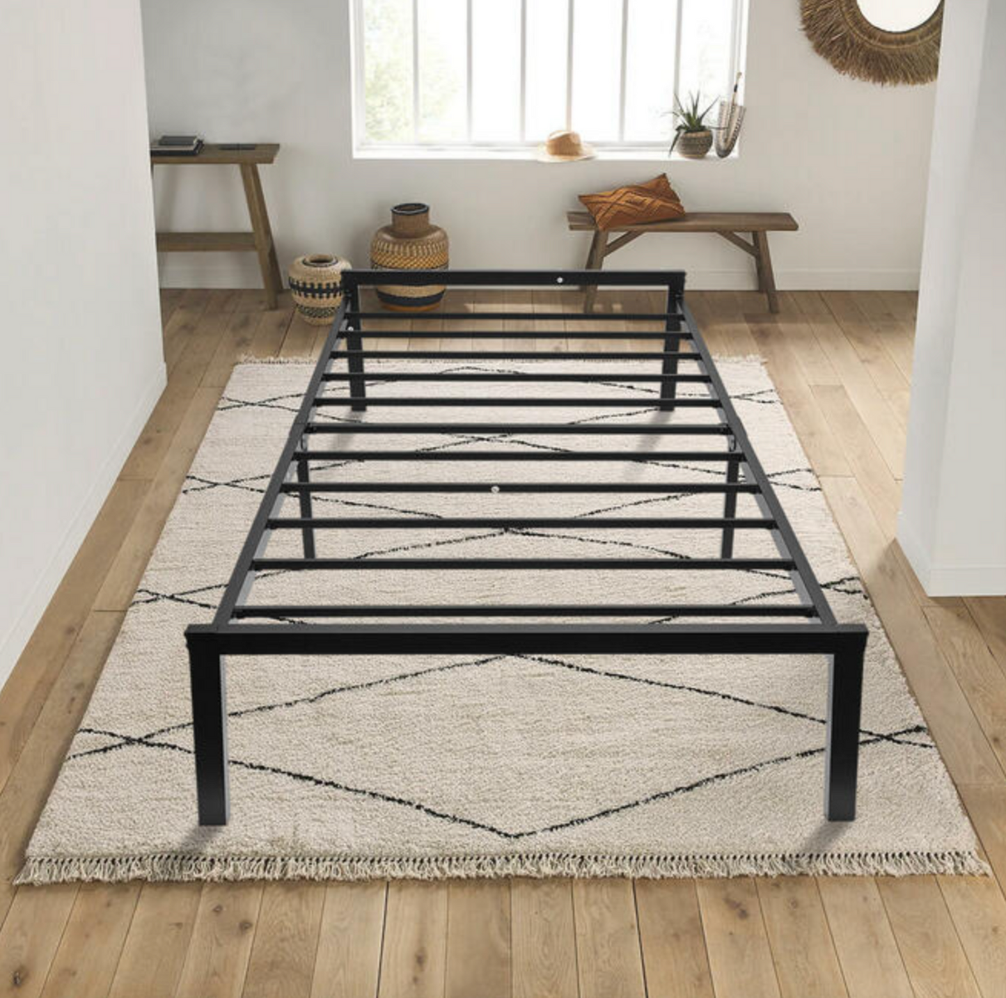 Black metal twin bed frame on cream rug in bedroom with bench and woven decor